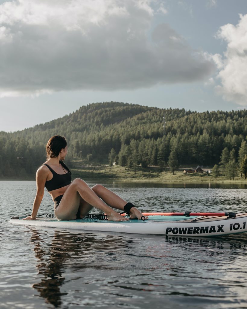A woman sitting on a paddleboard staring at the forest behind her in the distance