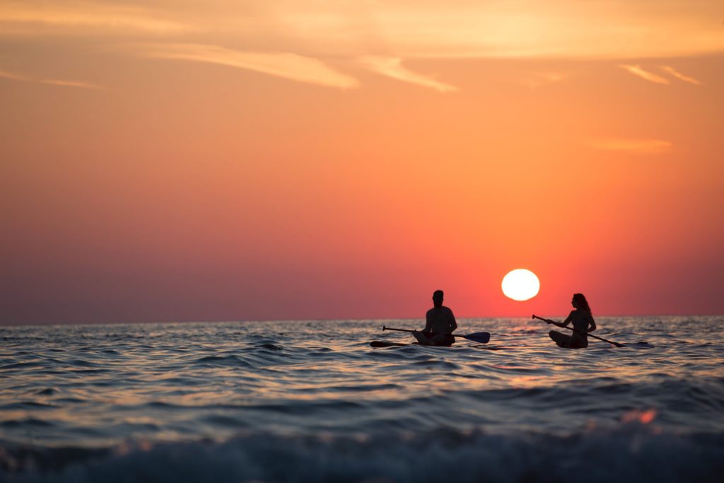 A man and a woman sitting on their paddleboards in the water at sunset